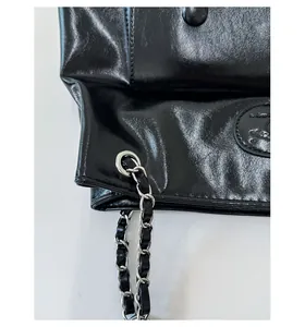 Close-up of black glossy oil-wax leather with silver eyelets and chain shoulder strap
