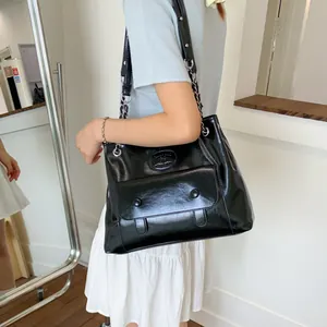 Large black glossy leather tote bag with chain strap shown on a female model