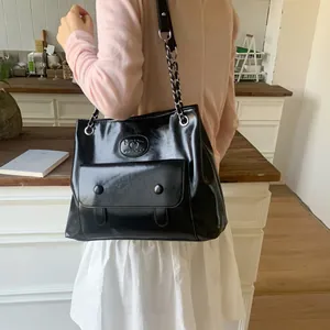 Vintage black patent leather tote bag with silver chain strap worn by a model