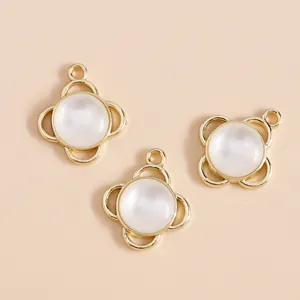 Detail of three clover-shaped gold charms with white cat-eye stones for DIY jewelry