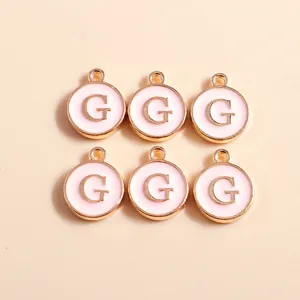 Detail of pink enamel and gold-plated alloy letter G round pendants for jewelry DIY