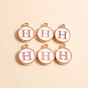 Close-up of pink enamel letter H round charms with gold-plated edges for DIY jewelry