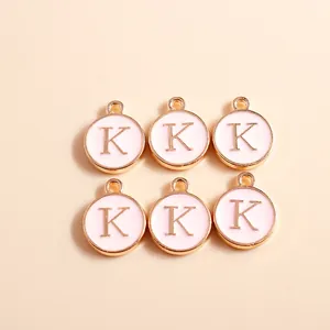 Detail of round gold-plated alloy letter K pendants with soft pink enamel finish