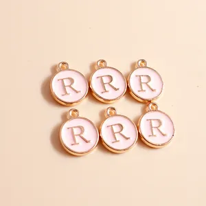 Detailed close-up of circular pink enamel and gold letter R charms for DIY jewelry making