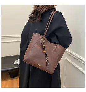 Detail of vintage brown leather tote bag with stylish charms and metal bell accessory