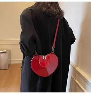 Red heart-shaped shoulder bag in shiny patent leather worn over a black blazer