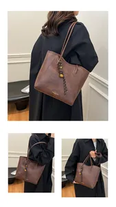 Detail of a brown textured leather tote bag with gold lettering and decorative bell charm