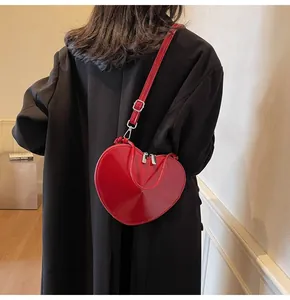 Detail showing high-gloss red heart-shaped patent leather crossbody bag with silver buckle