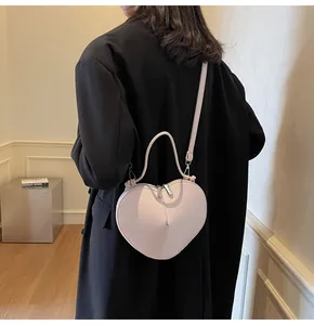 Model showing a stylish light pink heart-shaped crossbody bag with a matte leather texture