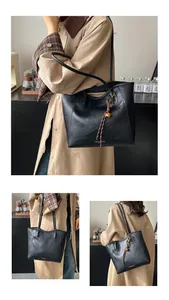 Detail of black PU leather tote bag with gold lettering and woven bell charm accessory