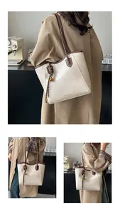 Detail view of large tote bag with cream leather, brown trim and gold bell charm