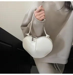 Detail of ivory heart-shaped crossbody bag with dual metal zippers and knotted strap
