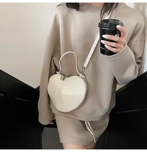 Detail of white heart-shaped crossbody bag with metal zipper and slender shoulder strap