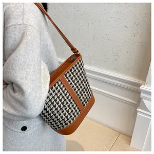 Detail of houndstooth bucket bag with brown leather trim worn with a grey coat