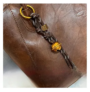 Close-up of brown textured leather tote bag with braided cord and golden bell detail