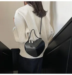 Detail of a black heart-shaped crossbody bag with glossy leather and silver zippers