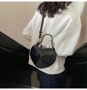 Detail of a black heart-shaped crossbody bag shown on a model in a modern indoor setting