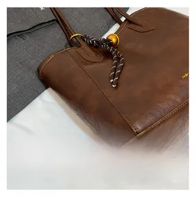 Detail of retro brown leather tote bag with braided knot and golden ball ornament