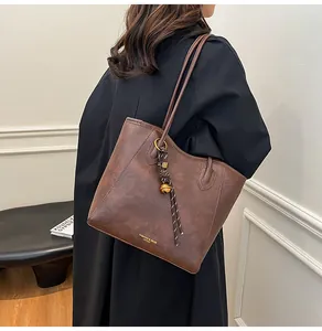 Detail of vintage brown tote bag with gold lettering and decorative pendant on black coat