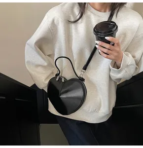 Detail shot of heart-shaped black crossbody bag with glossy finish on a casual outfit