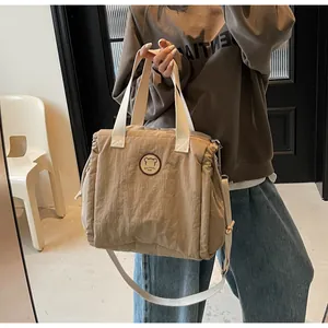 Dettaglio della borsa a tracolla in tela marrone chiaro con coulisse e patch orsetto