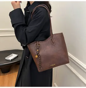 Detail of dark brown faux leather tote bag with gold bell and woven rope charm detail