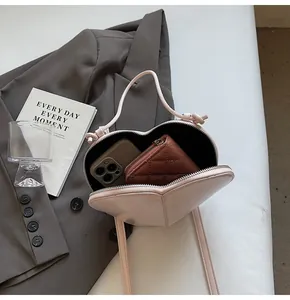 Detail shot of heart-shaped crossbody bag capacity with smartphone and wallet inside
