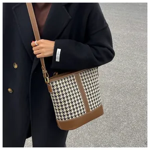 Detail of houndstooth bucket bag with brown leather trim and adjustable shoulder strap