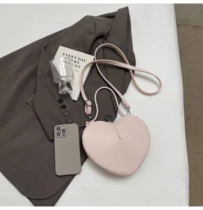 Pink heart-shaped crossbody bag shown with a smartphone to display the interior capacity
