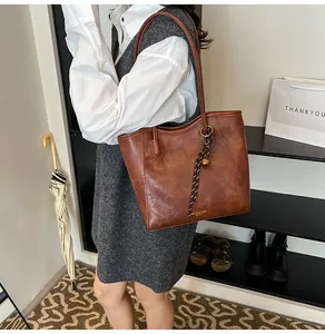 Detail of dark brown leather tote bag with braided lanyard and gold bell charm on a shoulder strap