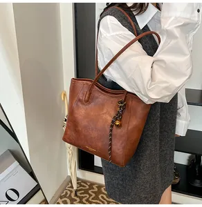 Detail of brown faux leather tote bag featuring woven charm and golden fashion lettering