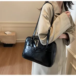 Dettaglio di una borsa tote nera lucida con logo Nornono portata a spalla da donna