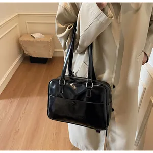 Dettaglio borsa a spalla in pelle nera lucida con logo goffrato su un trench kaki
