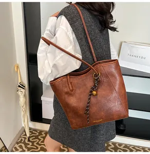 Detail view of caramel brown PU tote bag with elegant golden logo and decorative pendant