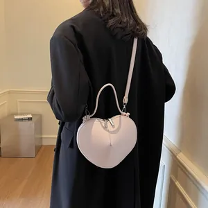 Pink heart-shaped leather crossbody bag with dual zippers shown on a black coat