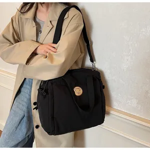 Dettaglio borsa a tracolla in nylon nero con logo in pelle marrone e tracolla in tessuto