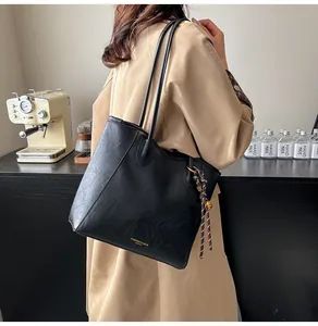 Detail of minimalist black leather tote bag with braided knot charm and slim shoulder straps