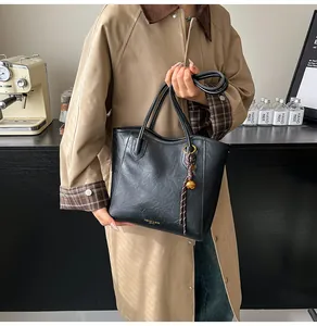 Detail of black faux leather tote bag with gold lettering and charm on casual coat