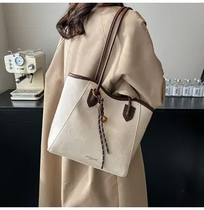 Detail of beige leather tote bag with brown straps and braided charm in casual setting