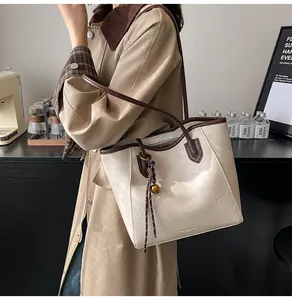 Chic beige tote bag with brown leather handles worn by a model in a cozy interior setting