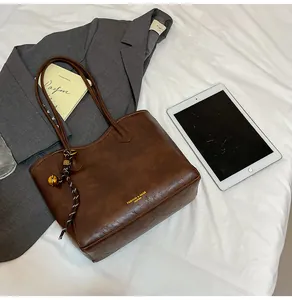 Close-up of dark brown PU leather tote bag with fashion logo and decorative gold bell charm