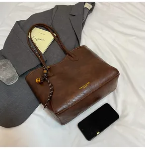 Close-up of brown vintage PU leather tote bag with gold lettering and decorative pendant