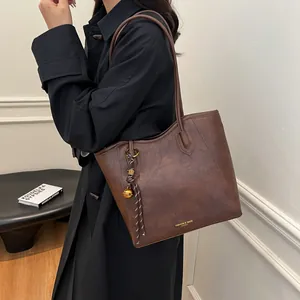 Classic dark brown tote bag with vintage texture and gold bell charm in a minimalist setting