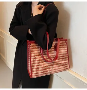 Detail of red houndstooth tote bag with leather straps on a model wearing a black coat