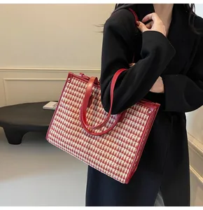 Detailed view of red houndstooth tweed tote bag with leather handles shown on a model