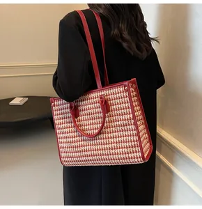 Detailed view of red houndstooth tote bag worn as a crossbody by model in indoor setting