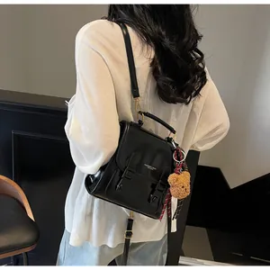 Detalle de mochila de cuero negro brillante con hebilla y colgante de oso decorativo