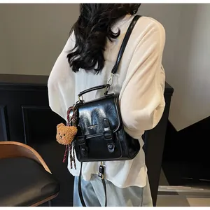Detalle del bolso de cuero negro brillante con correas de hebilla y amuleto de oso de peluche