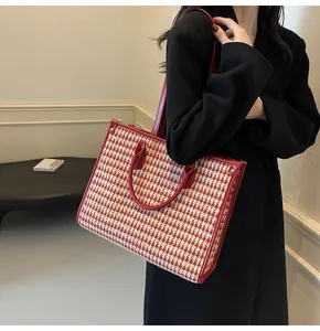 Detail of red houndstooth tote bag with leather straps worn over a black coat