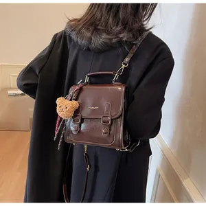 Detalle de mochila de cuero marrón oscuro con colgante de oso en modelo con blazer